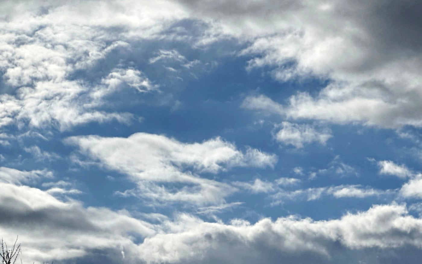 a blue sky seen through a hole in layers of white and grey cumulus clouds