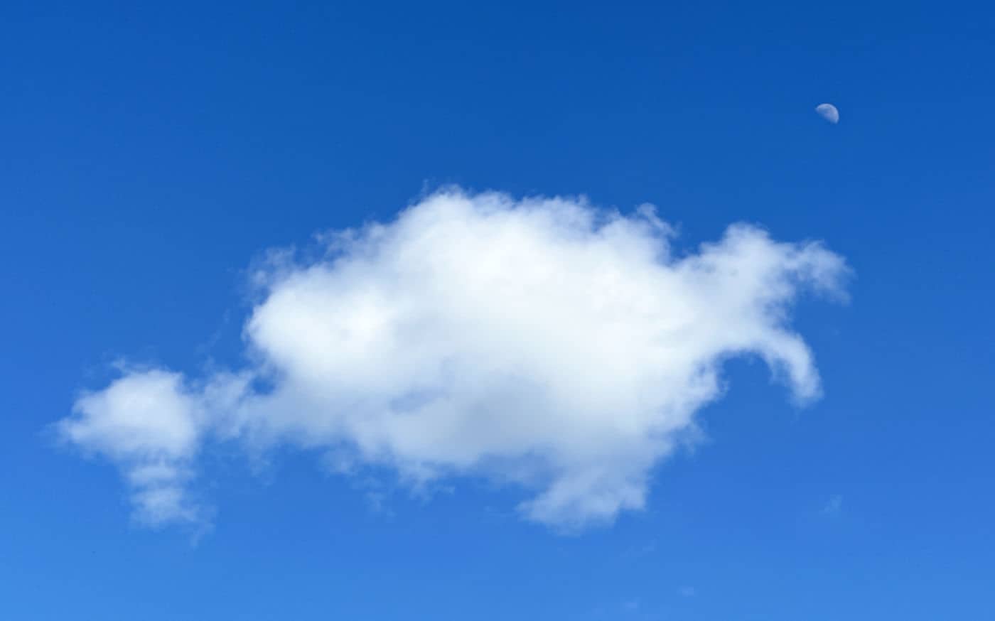 One small Cumulus cloud in a clear blue sky, with a first-quarter moon