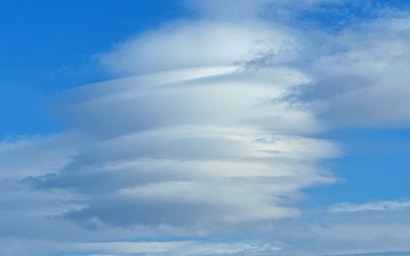 a stack of lenticular clouds in a mid-blue sky