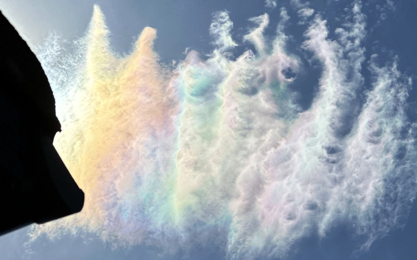 multi-coloured high cirrus clouds in a blue sky, with the sun just hidden behind the corner of a roof