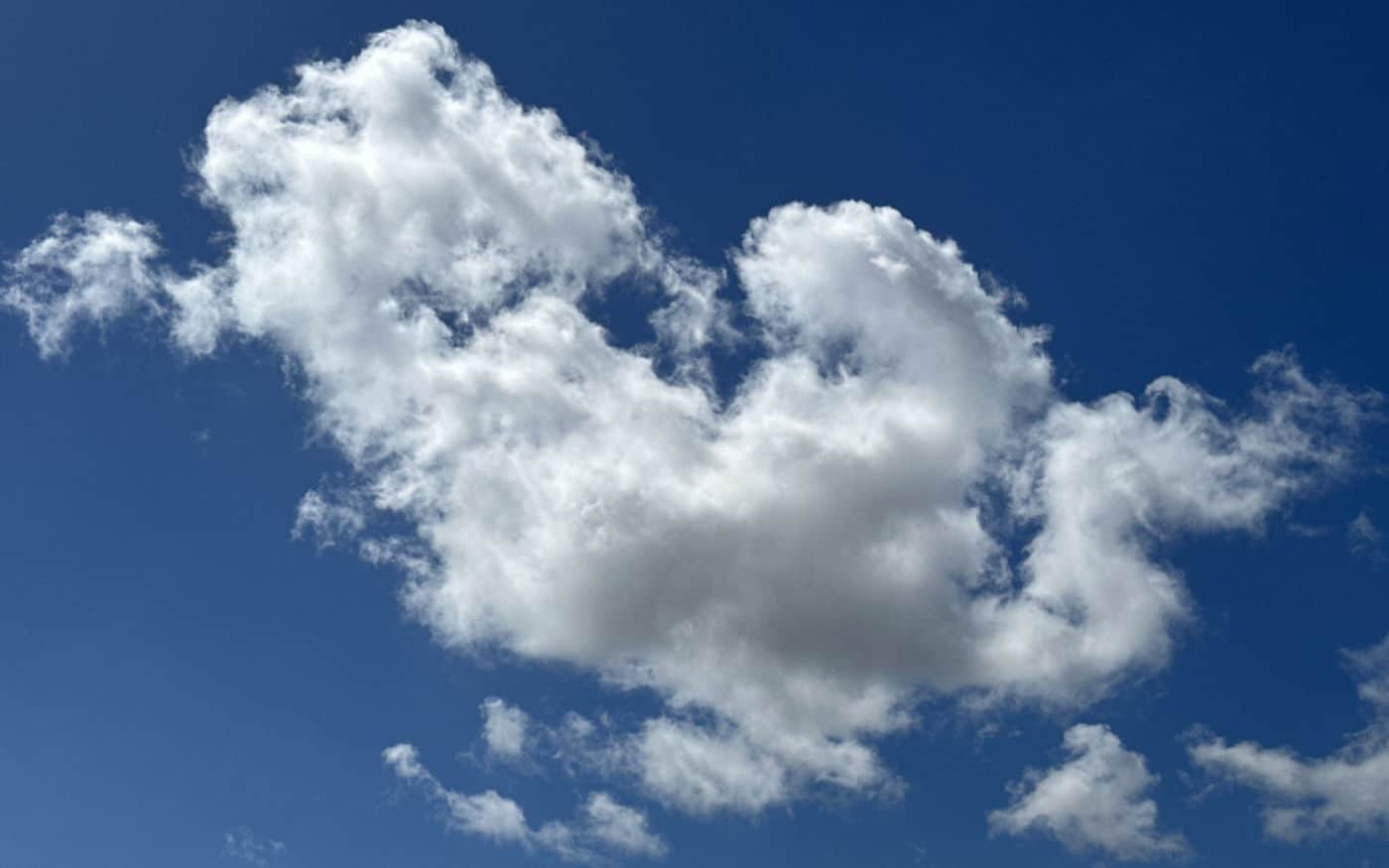 a deep blue sky seen between two patches of thin, puffy white clouds